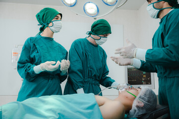 Group of male and female team of surgeon wearing scrub, mask and headscarf with gloves operating young woman in operation theatre in modern hospital