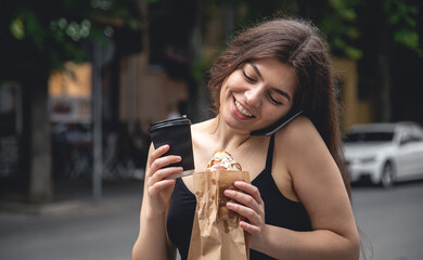 A young woman with a croissant and a cup of coffee on a city walk.