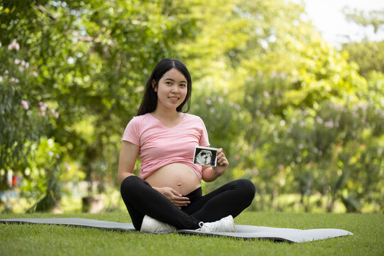 Asian pregnant woman holding ultrasound image in the garden
