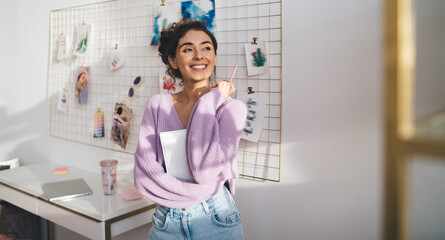 Gentle sweet girl in purple sweater posing at camera smiling sincerely from. Radiant brunette woman with beautiful appearance holds diary in hands. Positive female student with notebook organizer