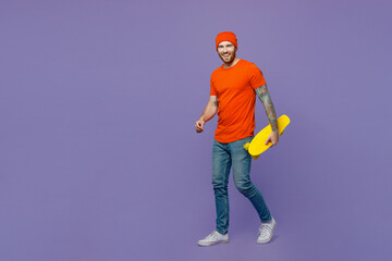 Full body side view smiling happy young european man 20s he wears red hat t-shirt hold pennyboard skateboard isolated on plain pastel light purple background studio portrait. People lifestyle concept.