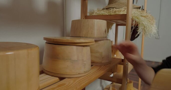 Woman arranges wooden molds for making hats in rows on shelf