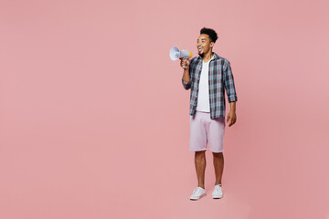 Fototapeta premium Full body young smiling man of African American ethnicity 20s wear blue shirt hold scream in megaphone announces discounts sale Hurry up isolated on plain pastel light pink background studio portrait.