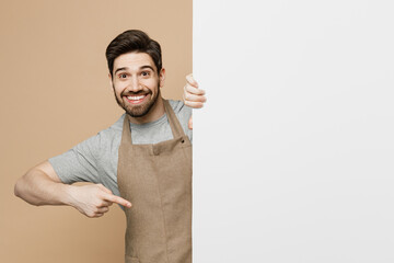 Young man barista barman employee wear brown apron work in coffee shop point big white billboard...