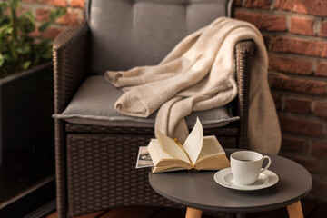 Morning coffee. Cozy interior: a cup of coffee and an open book on a table against the background of a wicker chair with a plaid. Leisure on the terrace in the garden.