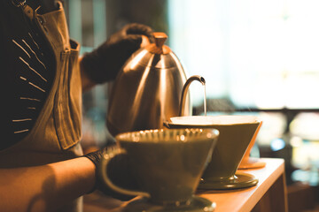 hipster barista making a drink coffee with drip or filter style by pouring hot water to brew a caffeine beverage from black bean in cafe restaurant business shop, using paper for aroma to a cup or mug