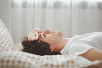 Man sleeping on bed with hand on his forehead on a bed, Sleepless Caucasian man suffering from insomnia. Headache and a severe cold guy. The concept of minor diseases and isolation.