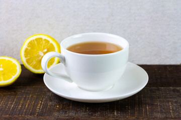 Cup of hot tea in white ceramic cup and fresh lemon on rustic wooden table and wihte background.