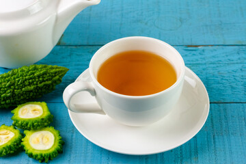 Bitter gourd or bitter melon tea in white cup on blue wooden background. Scientific name is Momordica charantia. As a whole food and herbs for treating diseases.