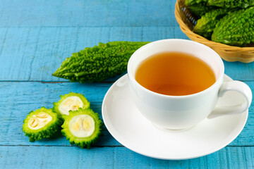 Bitter gourd or bitter melon tea in white cup on blue wooden background. Scientific name is Momordica charantia. As a whole food and herbs for treating diseases.