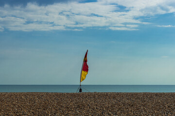 Fototapeta na wymiar Lifeguard flag on a shingle beach against a blue sky
