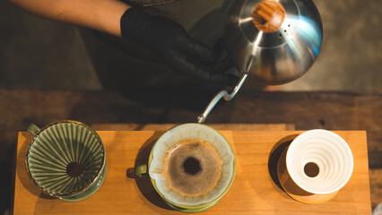 hipster barista making a drink coffee with drip or filter style by pouring hot water to brew a caffeine beverage from black bean in cafe restaurant business shop, using paper for aroma to a cup or mug