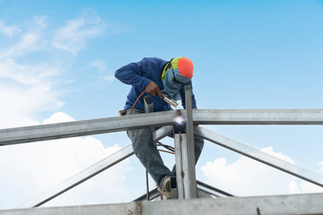 Construction worker : Welding of steel on top of roof structure core. Under the blue sky during the day when the sky is clear. No safety protection and falling from a height.