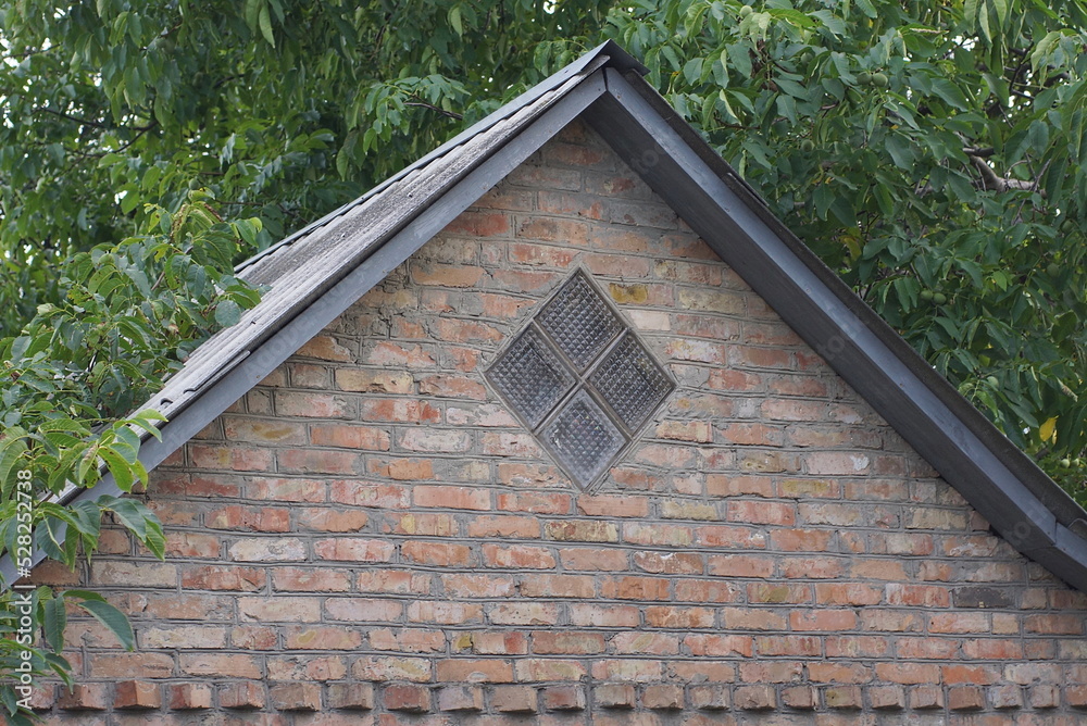 Poster old brown brick loft with a small one gray window against the backdrop of green vegetation on the street