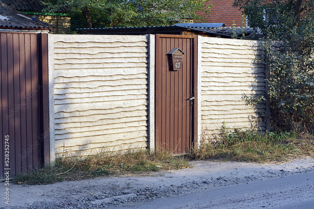 Poster one closed brown metal  door and part of the concrete gray wall fence on the street in the green grass