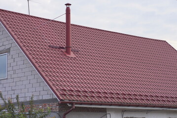 part of a white brick private house under a red tiled roof with a metal chimney against a gray sky