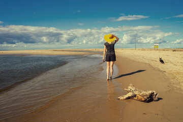 Dziewczyna w żółtym kapeluszu spacerująca po plaży. Pogodny słoneczny letni dzień, spokojna...