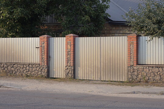 gray metal gate and a closed door on an iron fence wall on a stone foundation in a rural street