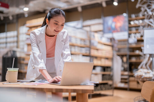 Asian Female Smart Entrepreneur Working Use Laptop Device Stock Manage And Checking Product Inventory In Warehouse Showroom,asia Woman Smiling Cheerful Business Owner Work In Showroom Warehouse Store