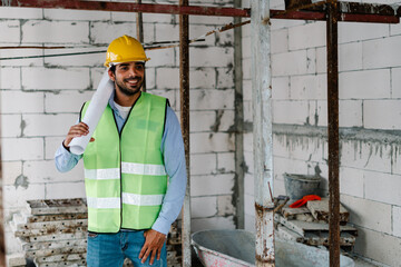 Construction worker in vest with safety helmet on head holding blueprint at construction site