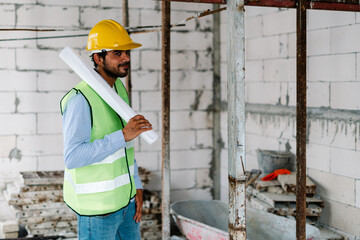 Construction worker in vest with safety helmet on head holding blueprint at construction site