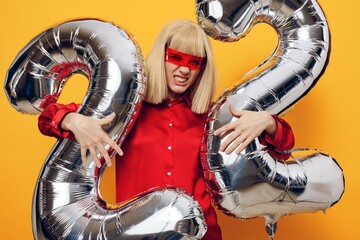 an emotional blonde woman stands on a yellow background in futuristic red glasses, in a red shirt...
