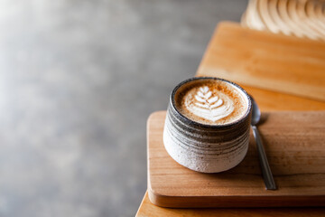Grey ceramic cup of cappuccino with latte art on wooden background.