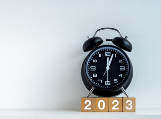 2023 Happy New year background. 2023 calendar number on wooden cube blocks with black alarm clock...