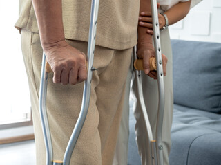Closeup elderly woman's hands holding on crutches standing in living room at home, trying to walk....