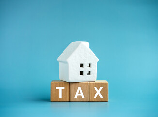 Home tax concept, residential or real estate property, land and building annual taxation. Word "TAX" on wooden cube blocks under the white small house model isolated on blue background, minimal style.