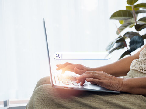 Online Searching Concept. Empty Blank Search Bar With Magnifying Glass Icon Appear While Hands Of Senior Woman Using Laptop Computer. Elderly Female With Internet. Older People And Technology.