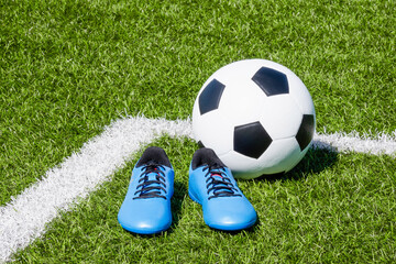 Soccer ball and pair of soccer football sports shoes cleats on green artificial turf football field...