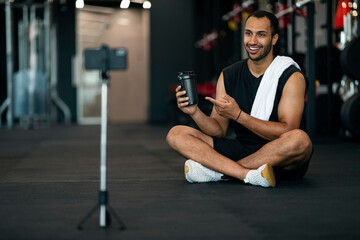 Fototapeta na wymiar Handsome Black Male Fitness Blogger Recording Video Review For Sport Shaker Bottle