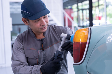 Professional car service male worker, with orbital polisher, polishing green classic vintage car in auto repair polishing shop