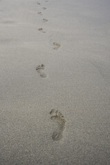 Fototapeta na wymiar Footprints of human feet on the gray sand of the beach or putyn