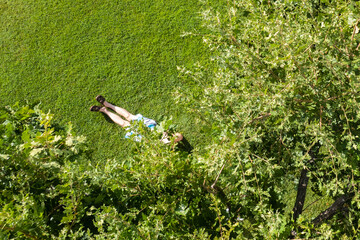 Сouple of woman an man lovers sitting on the green grass under tree in a park. Top view, drone, aerial view