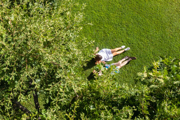 Сouple of woman an man lovers sitting on the green grass under tree in a park. Top view, drone, aerial view
