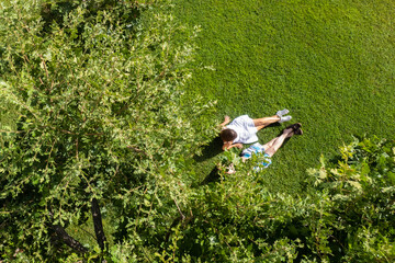 Сouple of woman an man lovers sitting on the green grass under tree in a park. Top view, drone, aerial view