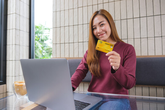 Portrait image of a young woman holding and showing credit cards while using laptop computer for online payment