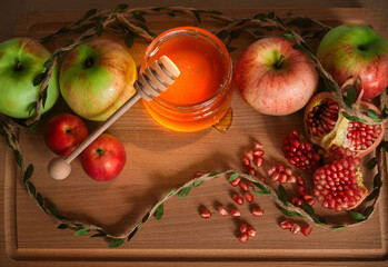 Red and green apples, pomegranate and honey in a glass jar on wooden background. Traditional Jewish new year food. Happy Rosh Hashanah concept.