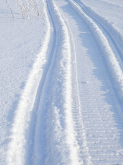 Track of traces from a snowmobile in drifts of white snow. Nature and outdoor on a winter sunny day. Vertical illustration with snowy field