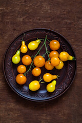 Brown ceramic plate with yellow cherry tomatoes and pear tomatoes on a yellow background. Organic natural food. Top view. Copy space.