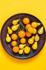 Brown ceramic plate with yellow cherry tomatoes and pear tomatoes on a yellow background. Organic natural food. Top view.