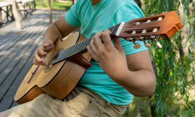 The young man plays hands and on a classic acoustic wooden guitar on the street. Focus close-up...