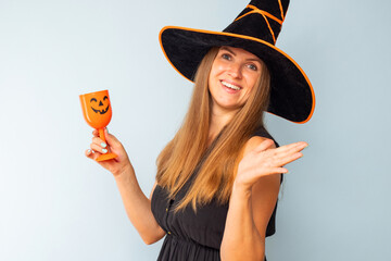 Happy Halloween! Happy brunette woman in halloween witch costume with black hat holding glass of...