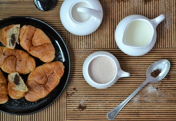 Coffee set with coffee and milk next to a plate of chocolate croissants