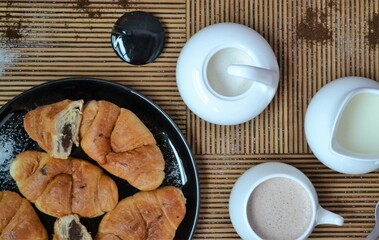 Coffee set with coffee and milk next to a plate of chocolate croissants