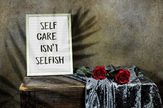 Self Care Isn't Selfish in wooden ornate picture frame photo with red roses flowers on wooden table with textile. vintage photo 