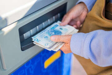 grandmother withdraws her pension at an ATM. A woman holds Polish money and zloty bills in her hands