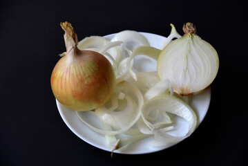 A white plate with chopped onions and an onion on a black background. Delicious onion close-up.